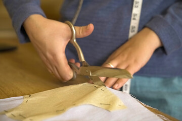 The fashion designer cuts the fabric according to patterns with scissors.