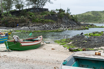 Lindas rochas da praia no Forte São Mateus em Cabo Frio, com a água do mar em volta delas, muitos barcos de pesca e muitos pássaros nas rochas.