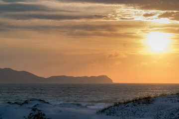 Lindo nascer do sol na Praia das Dunas, com algumas dunas de areia, lindo céu dourado e muitas montanhas ao fundo