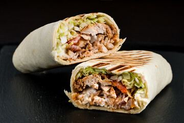 Fresh shawarma from chicken, tomatoes, lettuce, herbs, sauce and pita bread on a dark background. - 548335065