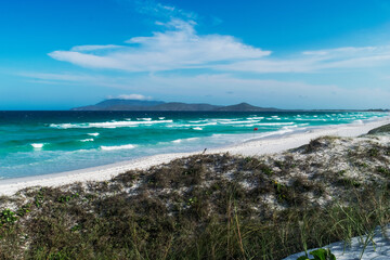 Orla do Chateau Recanto das Dunas na Praia das Dunas, com algumas dunas de areia céu azul e muitas montanhas ao fundo.