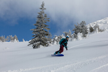 An active girl rides on a snowboard freeriding on a snowy slope in a backcountry alpine terrain in white mountains