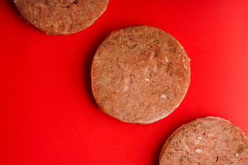 Appetizing large frozen patties ready for frying lie on a red background