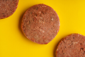 Frozen meat patties ready for frying lie on a yellow background, close-up