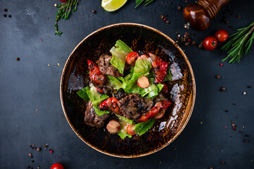 Fresh salad with beef medallions, roasted peppers, tomatoes, lettuce and dressing on a plate.