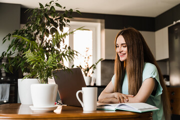 Young woman have a break, watching online videos and trainings on laptop, preparing for conference. Cheerful girl with laptop typing text and chatting with friends and family in at home.