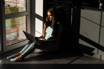 Cheerful young woman programmer works remotely on laptop and try to meet deadline at home. Candid girl with laptop is smiling and rejoices at successful work in IT company.