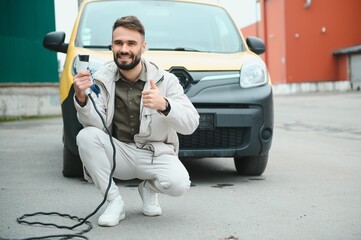 Portrait of a young man standing with charging cable near the charging station