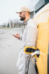 Casual man near electric car waiting for the finish of the battery charging process