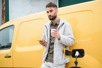 Casual man near electric car waiting for the finish of the battery charging process