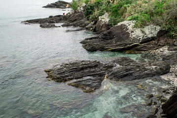 Praia no Forte São Mateus com a cidade de Cabo Frio ao fundo, muita vegetação rasteira e rochas...