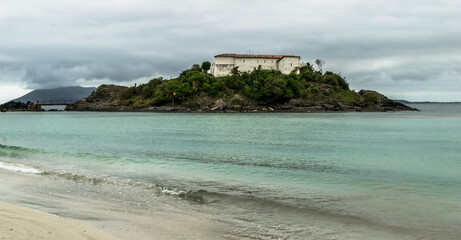 Obraz premium Praia do Forte, com o forte no topo de monte, mar, grandes rochas e céu com nuvens.