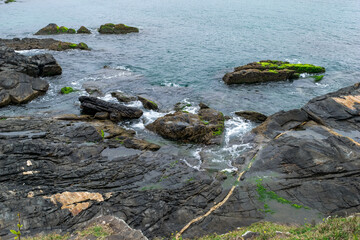 Rochas na praia no Forte São Mateus, com a água azul do mar entrando entre elas.