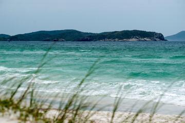 Obraz premium Vista da orla da Praia das Dunas, com lindo mar, céu azul e muitas montanhas ao fundo.