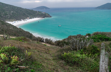 Vista de cima da linda Praia Arraial do Cabo Atalaia, com suas areias brancas, um lindo mar em volta, muita vegeta&ccedil;&atilde;o ao redor e cercada de grandes montanhas verdes.