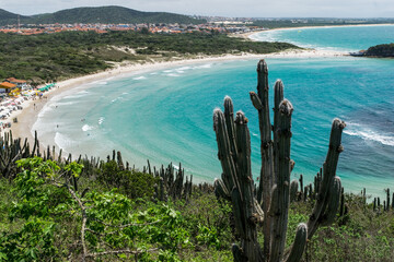 Vista de cima da linda praia das Conchas, próxima a cidade de Cabo Frio, com muitos quiosques a beira-mar, mar com águas limpas e em tom de verde e azul, com montanhas ao fundo.