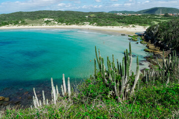 Vista de cima da linda praia das Conchas, pr&oacute;xima a cidade de Cabo Frio, com quiosques a beira-mar, c&eacute;u azul, mar com &aacute;guas limpas e em tom de verde e azul, com montanhas ao fundo.