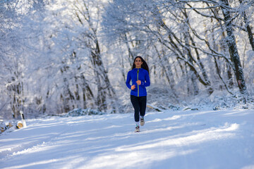 Sportswoman running in nature at snowy winter day. Winter fitness concept.