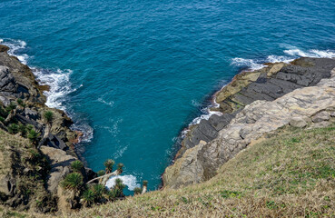 Vista de parte da linda praia das Conchas, com vegetação rasteira, um lindo mar azul em volta, muitas rochas e montanhas ao fundo.