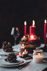 Rustic table decor for Christmas or New Year family dinner. Centrepiece with red candle, dry orange, cone, cinnamon, anise. Zero waste eco-friendly home. Cozy atmosphere, dark background. Close up