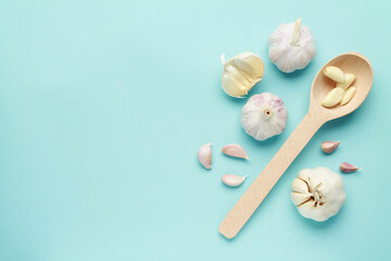 Fresh white unpeeled head bulb of garlic cloves on blue color background with wooden spoon. Vegan, organic, vitamins. Natural antibiotic, antioxidant, Allicin. Top view. Flat lay. Copy space for text