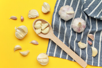 Fresh unpeeled head bulb of garlic and garlic cloves on yellow blue cloth fabric background with wooden spoon. Vegan, organic, vitamins. Natural antibiotic, antioxidant, Allicin. Top view. Flat lay