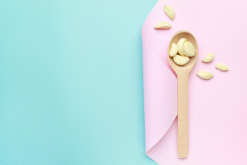 Fresh white garlic cloves on wooden spoon on pink blue color background. Vegan, organic, vitamins. Natural antibiotic, antioxidant, Allicin. Top view. Flat lay. Copy space for text