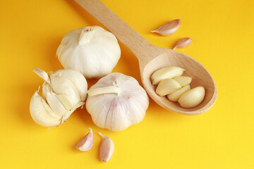 Fresh white unpeeled head bulb of garlic and garlic cloves on yellow color background with wooden spoon. Vegan, organic, vitamins. Natural antibiotic, antioxidant, Allicin. 