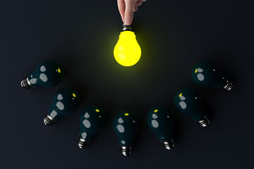 A hand holds a lit light bulb in the background of other extinguished light bulbs. The concept of...