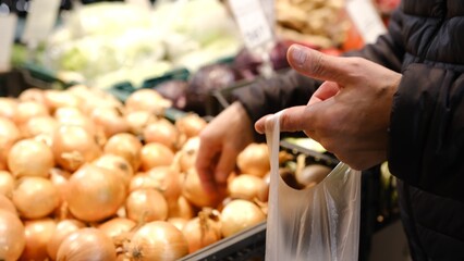 A man's hands choosing onion at the food market. Man take onion from thr stall in a food market. Man chosing vegetables in market