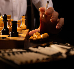 Player hand with half-smoked cigarette on table near chessboard