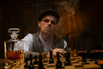 Young British gangster drinking whiskey, smoking and playing chess in bar