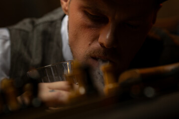 Man with glass of drink leaning on table and blowing cigarette smoke
