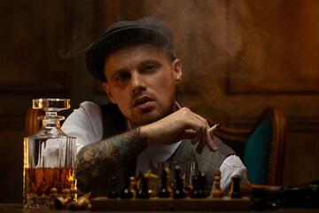 Young gangster smoking and drinking alcohol while playing chess - obrazy, fototapety, plakaty
