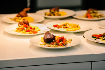 Close up of meat steak behind a of garnish vegetables and potatoes laid out on a plate and placed on a restaurant table before serving