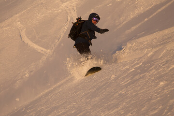 Freerider snowboarder running downhill in steep sunlight slope landscape. Fresh powder snow,...