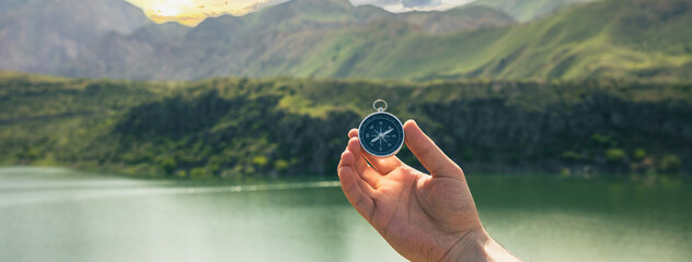 A man holds a compass against the backdrop of a lake