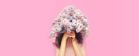 Portrait of woman covering her head with bouquet of fresh lilac flowers on pink background - Powered by Adobe