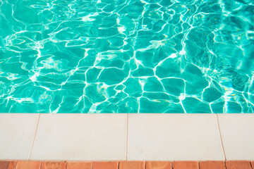 Swimming pool border. Close up edge of white cement floor near swimming pool with moving blue water.