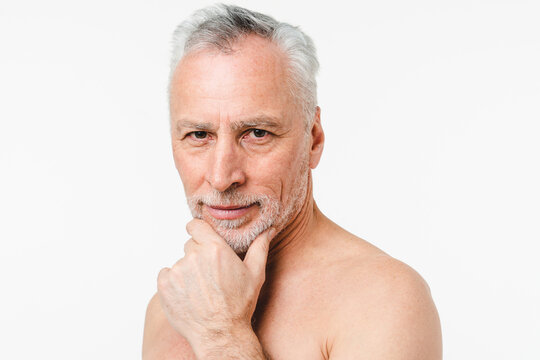 Cropped portrait of caucasian mature senior naked shirtless man preparing for shaving grey beard hair, touching his face, taking care of skin, applying aftershave isolated in white