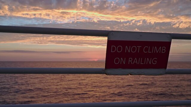 Pink sunrise in ocean. Safety sign foreground DO NOT CLIMB ON RAILING
