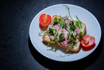 sandwich with bacon and microgreens and tomatoes on a black background