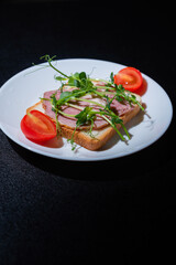 sandwich with bacon and microgreens and tomatoes on a black background