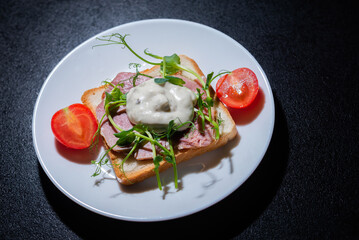 sandwich with bacon and microgreens and tomatoes on a black background