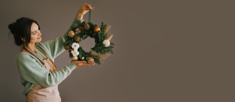 Millennial woman making Christmas wreath using natural pine branches and festive decorations in workshop banner. Small business - Powered by Adobe