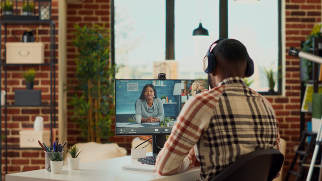 Young freelancer talking to coworkers on online videocall conference, attending remote business meeting on webcam at home. Using internet teleconference call to chat remotely at desk.