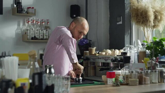 A male barista presses coffee in a templer and puts it in the coffee machine. The process of making aromatic espresso in a cafe. High quality 4k footage