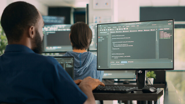 African american system engineer working on software development with source code, looking at computer. IT app developer writing ai algorithm in office, online cloud computing. Handheld shot.