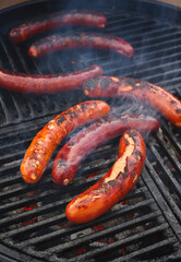 Traditionelle deutsche Bratwurst vom Grill angeboten als close-up auf einem Holzkohlegrill mit Feuer und Rauch 