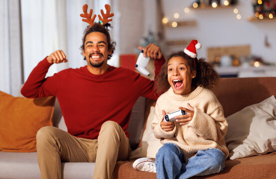 African american family father and daughter laugh and play video games together using a video game console on christmas holiday